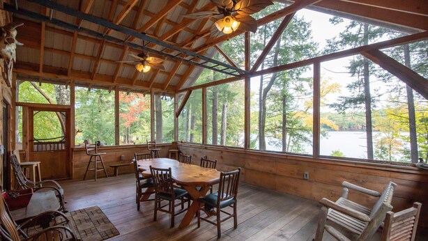 A wooden dining area with a large table and chairs, large windows with a view of trees, and ceiling fans.