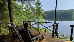 A wooden deck with two lounge chairs overlooking a calm lake, surrounded by dense forest.