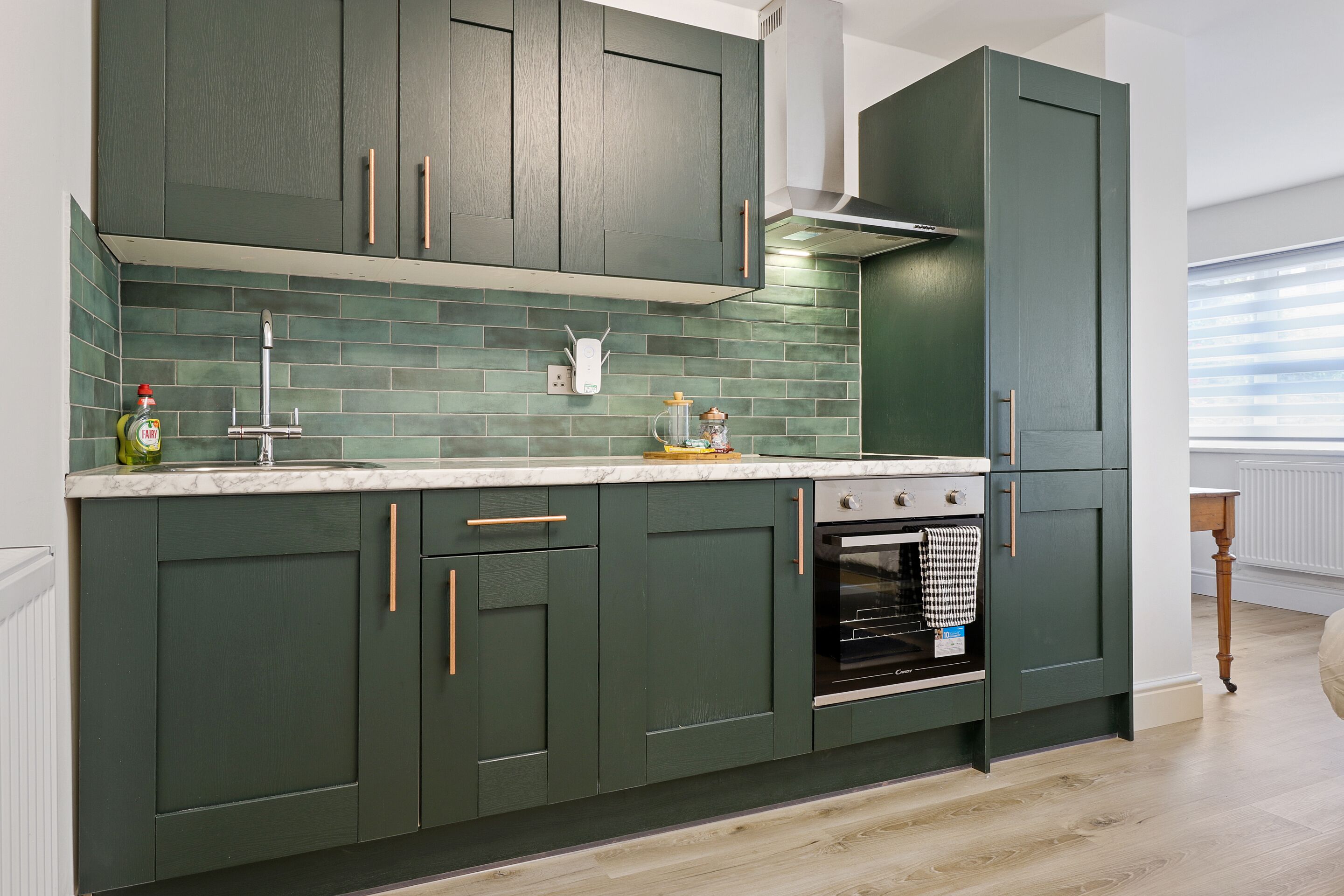 A modern kitchen with dark green cabinets, a white marble countertop, and a built-in oven.