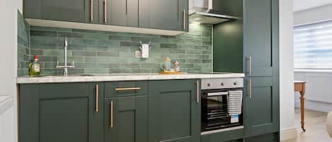 A modern kitchen with dark green cabinets, a white marble countertop, and a built-in oven.