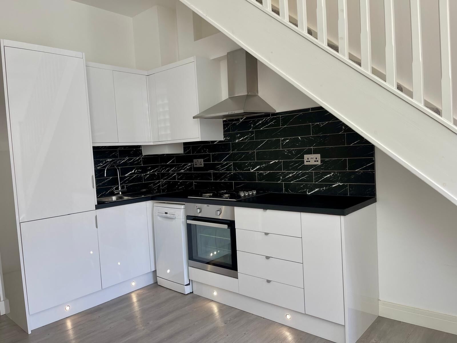 A modern kitchen with white cabinetry, black marble backsplash, and a built-in oven.