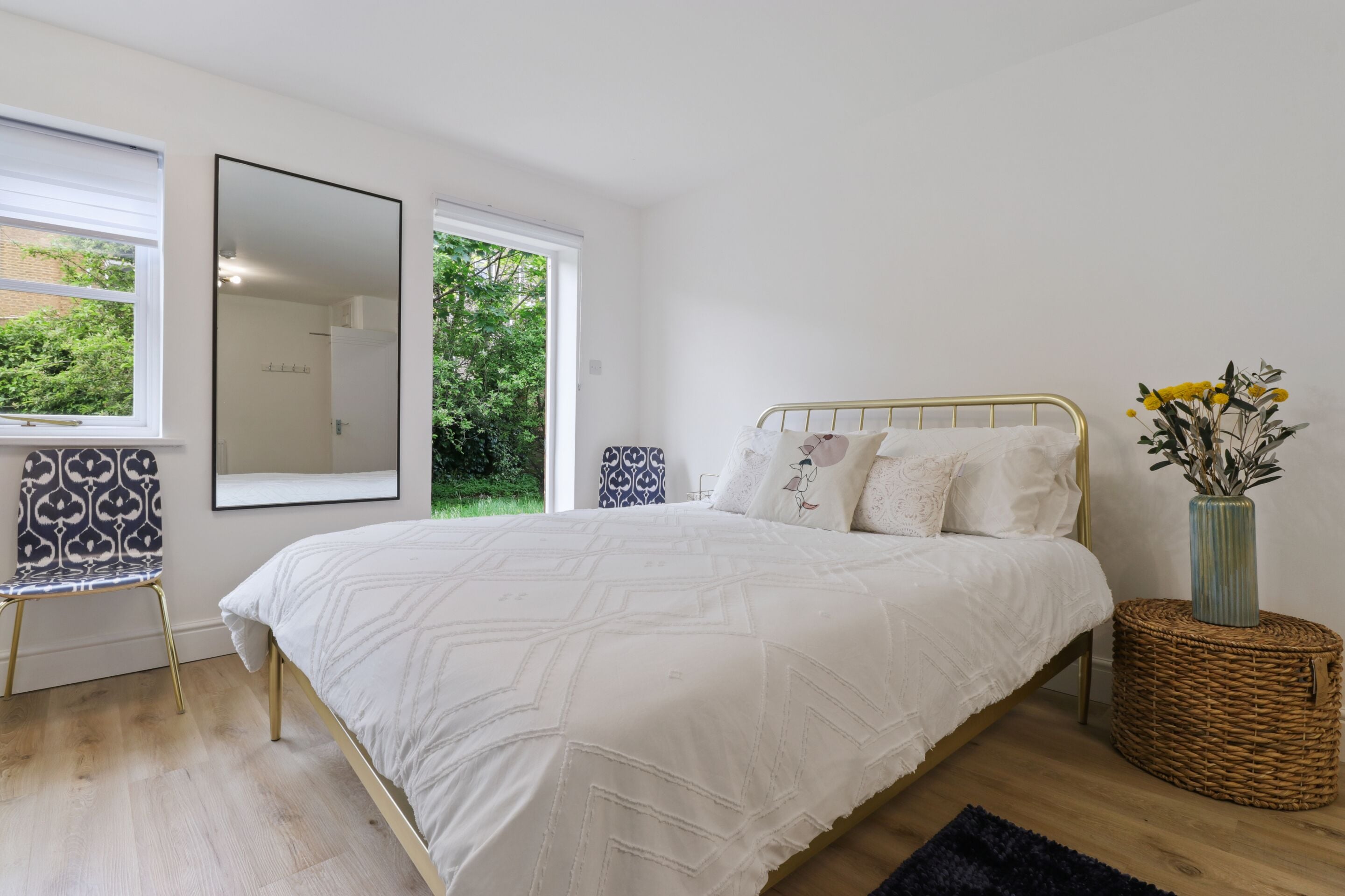 Ein Schlafzimmer mit einem großen Bett, einem Spiegel, einem Sessel und einem Fenster mit Blick auf Grünflächen.