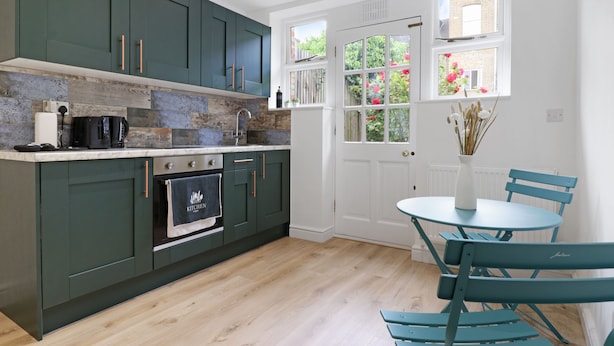 Una cocina moderna con gabinetes verdes, horno empotrado y comedor con mesa redonda y sillas color turquesa.