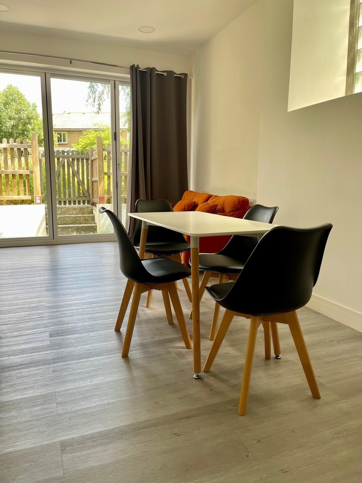 A dining area with a table and chairs, a sliding glass door leading to a balcony, and a view of a wooden fence and greenery.