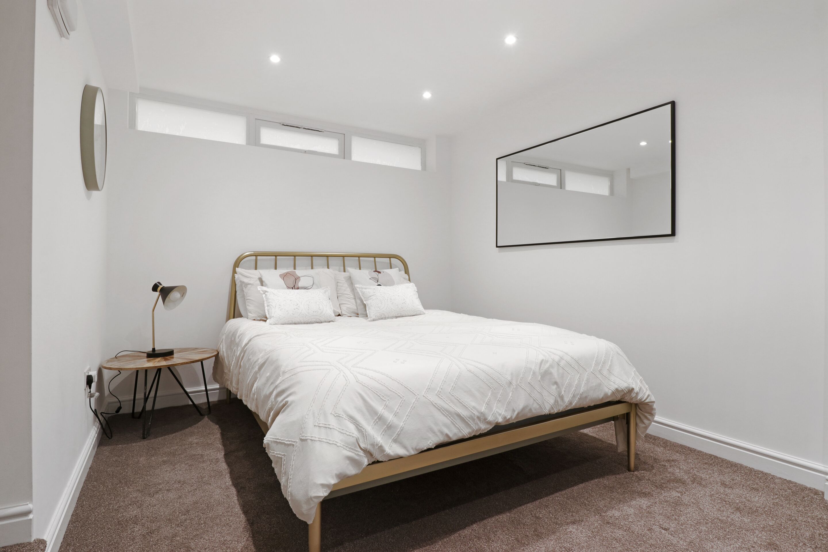 Een slaapkamer met een bed, nachtkastje, lamp en een grote spiegel aan de muur.