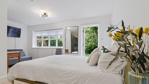 Un dormitorio con cama, televisión, ventana con vistas a la vegetación y un jarrón con flores.