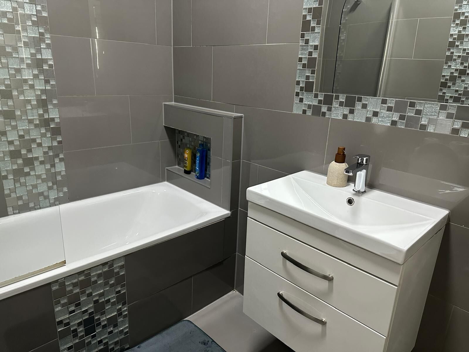 Ein modernes Badezimmer mit einer weißen Badewanne, einem Waschtisch mit Spiegel und einer gefliesten Rückwand.