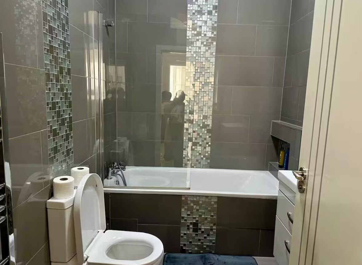 Un baño con inodoro, cabina de ducha de vidrio y pared revestida de mosaicos.