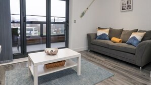 A modern living room with a grey sofa, a white coffee table, and a large sliding glass door leading to a balcony. - Seashell (Hornsea)