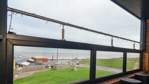 A view from a window overlooking a road with a grassy area and a building in the distance. - Seashell (Hornsea)