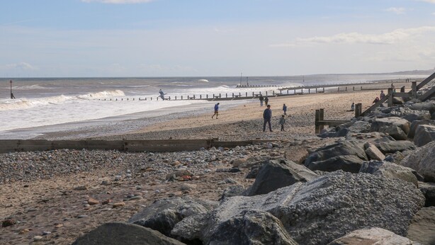 A rocky beach with a wooden pier extending into the sea, a sandy shore, and waves crashing onto the rocks. - Seashell (Hornsea)