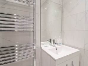 Ein modernes Badezimmer mit Duschkabine aus Glas, einem weißen Waschbecken mit Spiegel und Marmorfliesen.