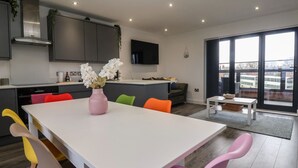 A modern kitchen with a white table, colorful chairs, and a pink vase with flowers. - Seashell (Hornsea)