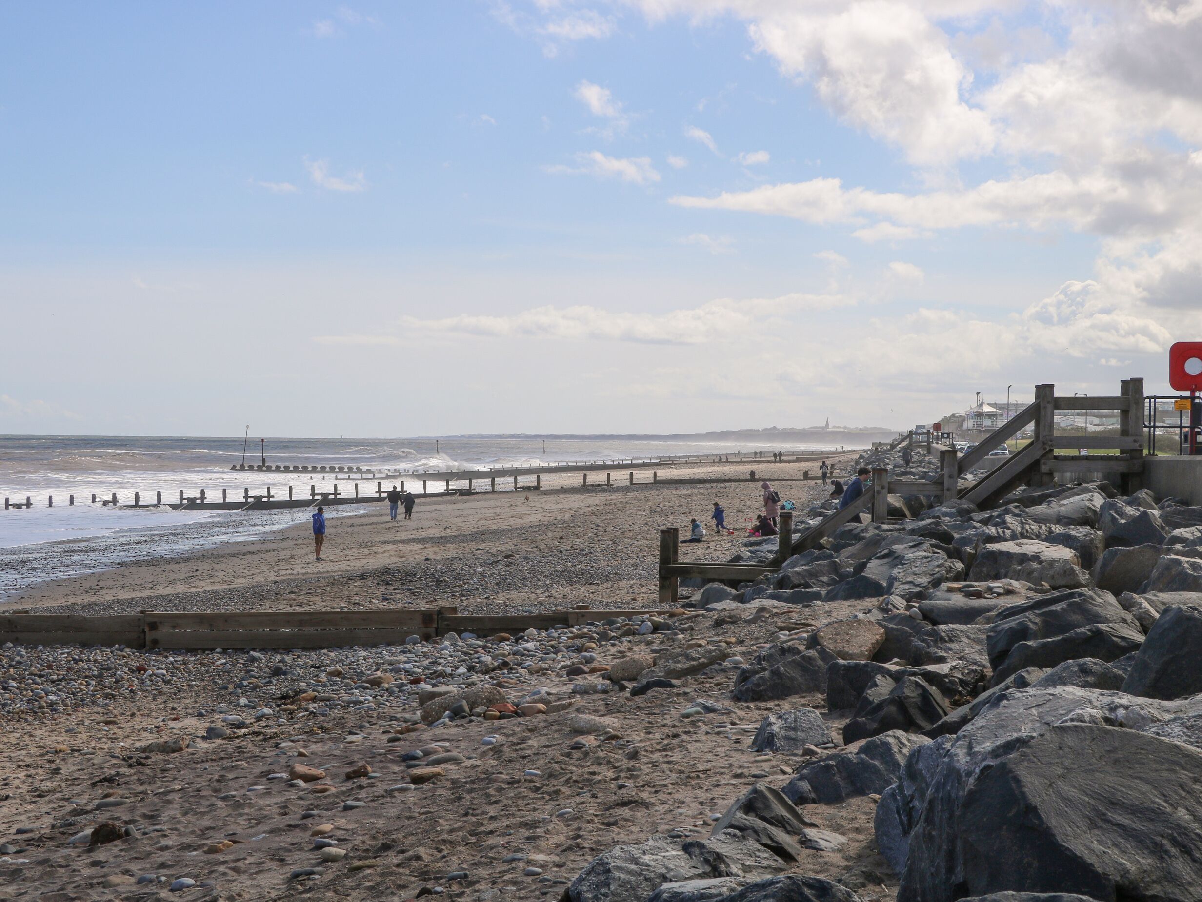 Une plage rocheuse avec une promenade en bois et une jetée en arrière-plan.