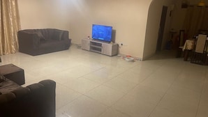 A living room with a TV on a stand, a sofa, and a tiled floor. - ELITE HOME STAYS (Lusaka)