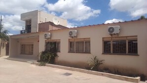 A two-story building with multiple air conditioning units, a satellite dish, and a small garden area. - ELITE HOME STAYS (Lusaka)