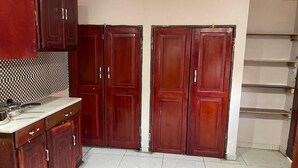 A kitchen with wooden cabinets, a countertop, and a tiled floor. - ELITE HOME STAYS (Lusaka)