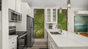 A modern kitchen with white cabinetry, stainless steel appliances, and a large island with a sink. - Remodeled #56,  AC, grnd flr end unit, ideal location! (Koloa)