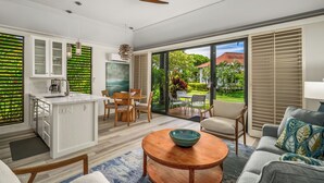 A modern kitchen with a central island, dining area with chairs, and a large sliding glass door leading to a garden. - Remodeled #56,  AC, grnd flr end unit, ideal location! (Koloa)
