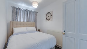 A neatly made bed with white linens, a headboard, and a bedside table with a lamp. - Remarkable 3-bed House in Middleton Manchester (Manchester)