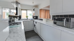 A modern kitchen with white cabinets, a marble countertop, a built-in washing machine, and a stainless steel microwave. - Remarkable 3-bed House in Middleton Manchester (Manchester)