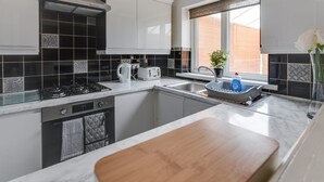 A modern kitchen with white cabinets, black and white tiles, a gas stove, a sink, and a window with a view of the outside. - Remarkable 3-bed House in Middleton Manchester (Manchester)