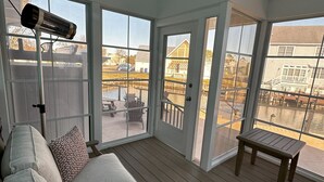 Een zonnedoorschoonde kamer met een houten terras, een bank met opvallende kussens, en een ventilator.