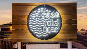 En neonskilte med teksten "casa del mar" mod en træbaggrund.