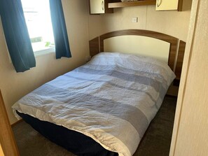 Ein Einzelbett mit Holz-Kopfstück in einem Zimmer mit beigen Wänden und einem Fenster mit Vorhängen.