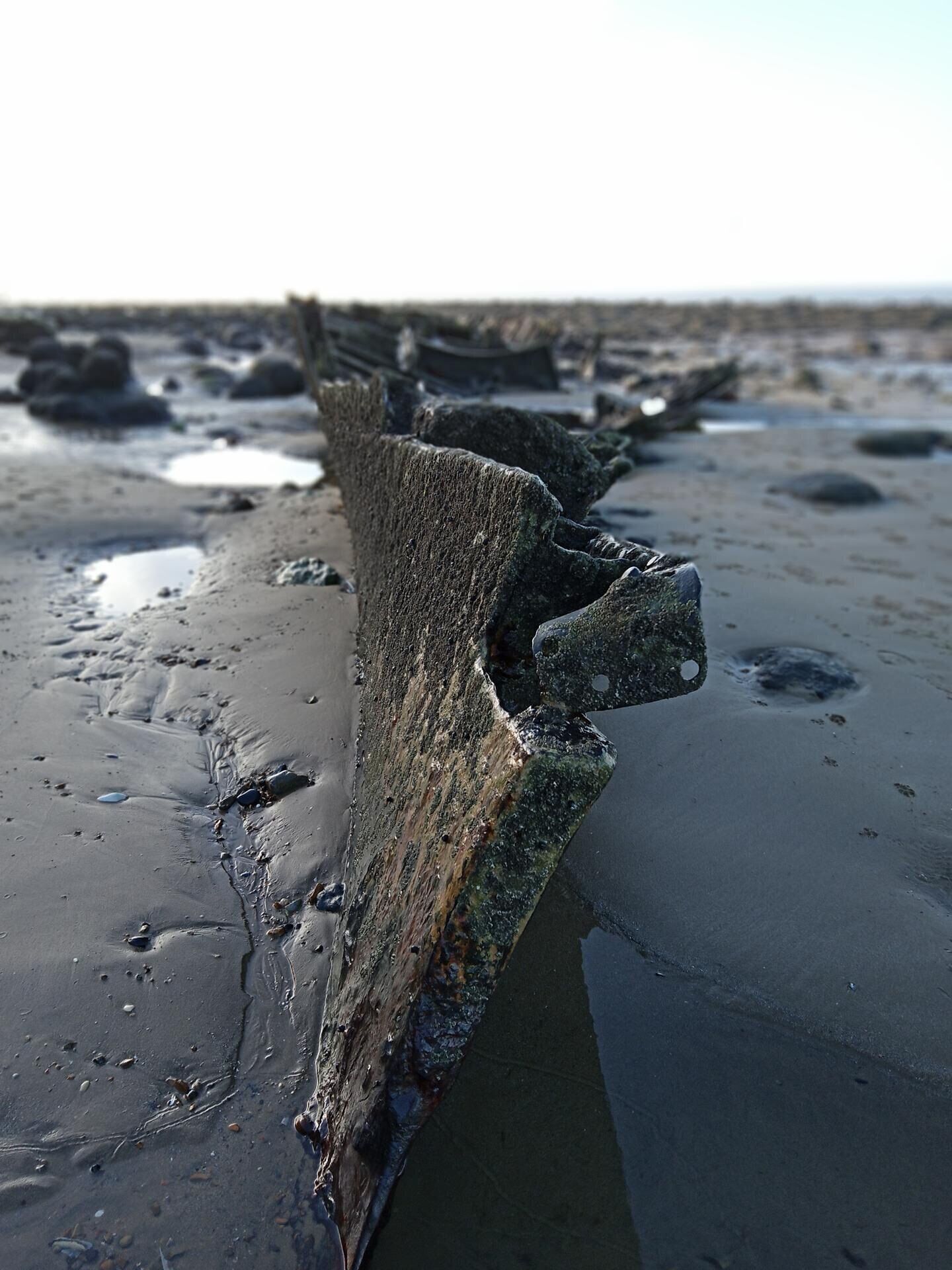 A large, weathered rock formation on a sandy beach with visible erosion patterns.