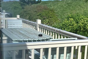 Eine Holzterrasse mit Geländer, mit Blick auf einen üppigen, grünen Hang.