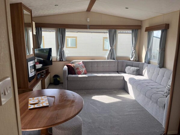 Interior acogedor de una casa rodante con sofá, televisor y mesa de comedor.