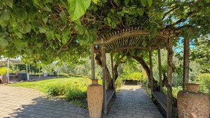 Une pergola avec un chemin en briques menant à celle-ci, le tout entouré de verdure.