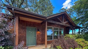 A wooden house with a green door, large windows, and a porch.