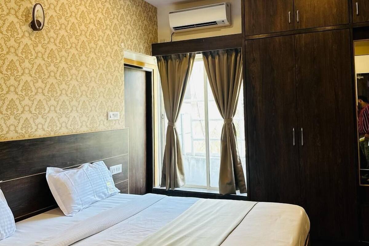 A hotel room with a bed, a ceiling fan, an air conditioning unit, and a window with curtains.