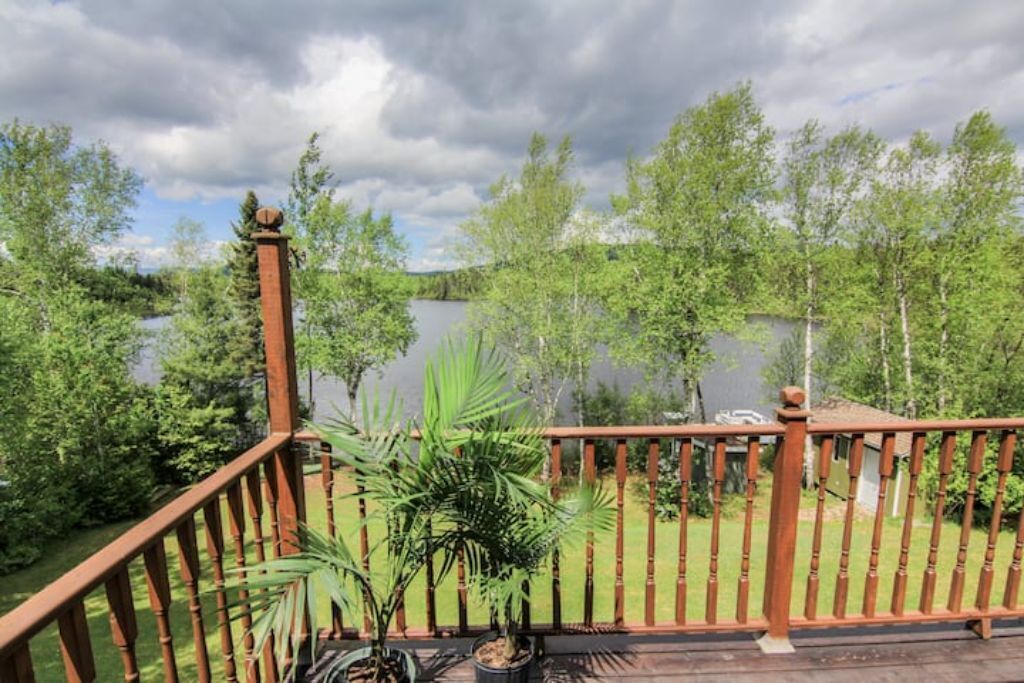 Une terrasse en bois avec une rambarde donnant sur un lac, entourée d’arbres.