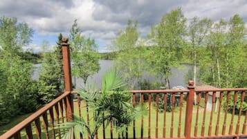 Une terrasse en bois avec une rambarde donnant sur un lac, entourée d’arbres.
