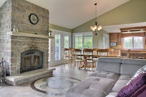 A spacious living room with a stone fireplace, a dining area with wooden chairs, and a kitchen with wooden cabinets.