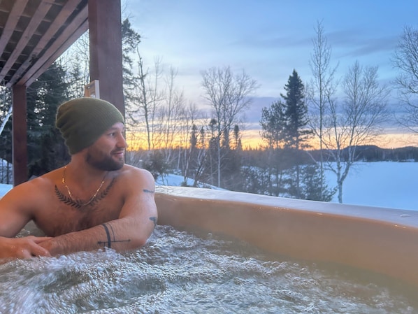 A person in a hot tub with a view of a snowy landscape and trees.