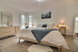 A bedroom with a bed, bedside lamps, a dresser, a mirror, and a painting on the wall.