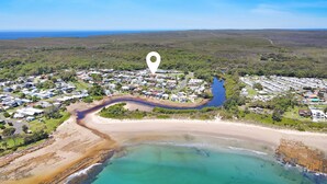 An aerial view of a coastal area with a river flowing through a residential community, surrounded by greenery and a beach. - Sylvia​’​s at Currarong – peaceful retreat (Currarong)
