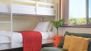 A bunk bed room with a window, a plant, and a sofa with cushions.