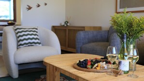 A cozy living room with a wooden coffee table, a floral vase, and a wine bottle. - Sylvia​’​s at Currarong – peaceful retreat (Currarong)