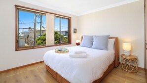 A bedroom with a large window, a bed with white linens, two pillows, a bedside table with a lamp, and a tray with towels. - Sylvia​’​s at Currarong – peaceful retreat (Currarong)