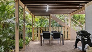 Une terrasse extérieure dotée d’une pergola en bois, de deux chaises noires et d’un barbecue.