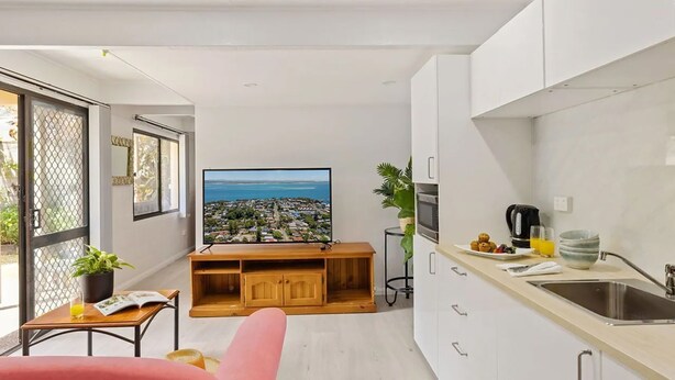 Un appartement moderne doté d’une cuisine, d’un coin repas et d’un grand téléviseur qui diffuse des images d’un paysage magnifique.