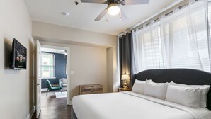 A hotel room with a large bed, a ceiling fan, a TV on the wall, and a view of the outside through the window.