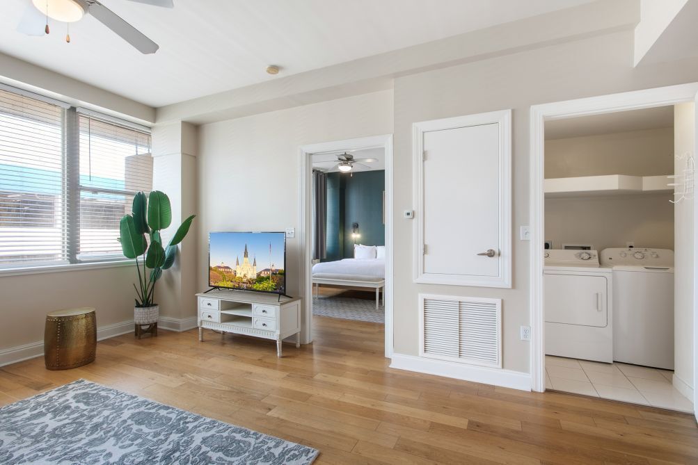A modern bedroom with a bed, a TV, a ceiling fan, and a laundry area.