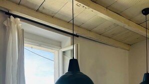 A room with a table, chairs, a hanging pendant light, a window with a view of the sea, and a curtain. - Maison vue Mer , Proche Bastia (Bastia)