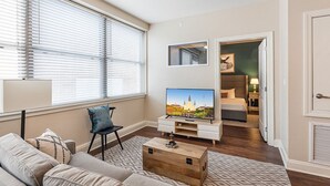 Une chambre d’hôtel moderne dotée d’une grande fenêtre, d’un téléviseur à écran plat, d’un canapé, d’une table basse en bois et d’un lit avec une table de chevet.